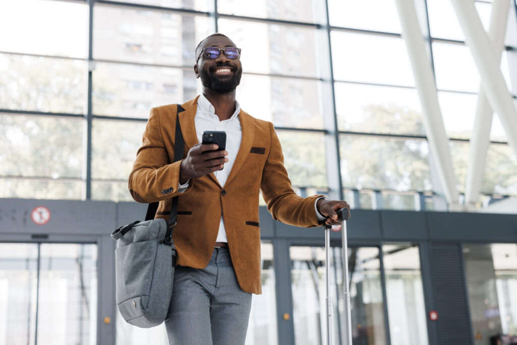 Man smiling while walking with a suitcase and phone, embodying calm, confidence, and freedom.