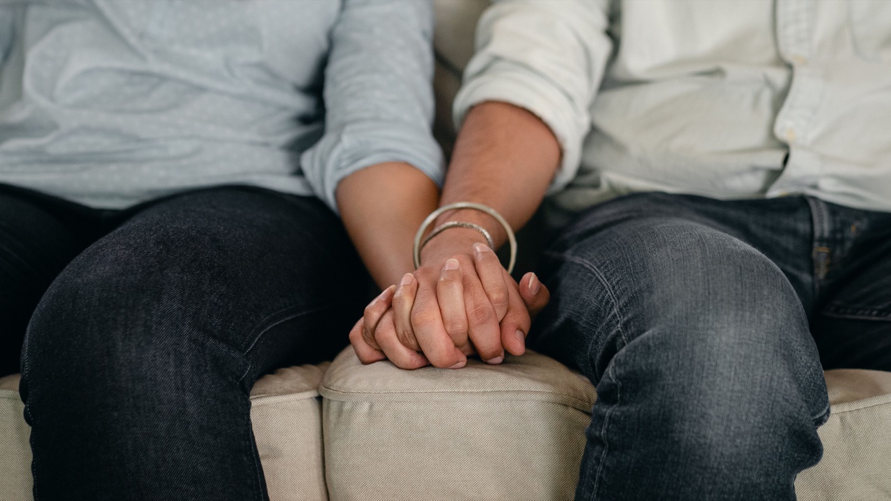 Two adults holding hands while seated together on a sofa.