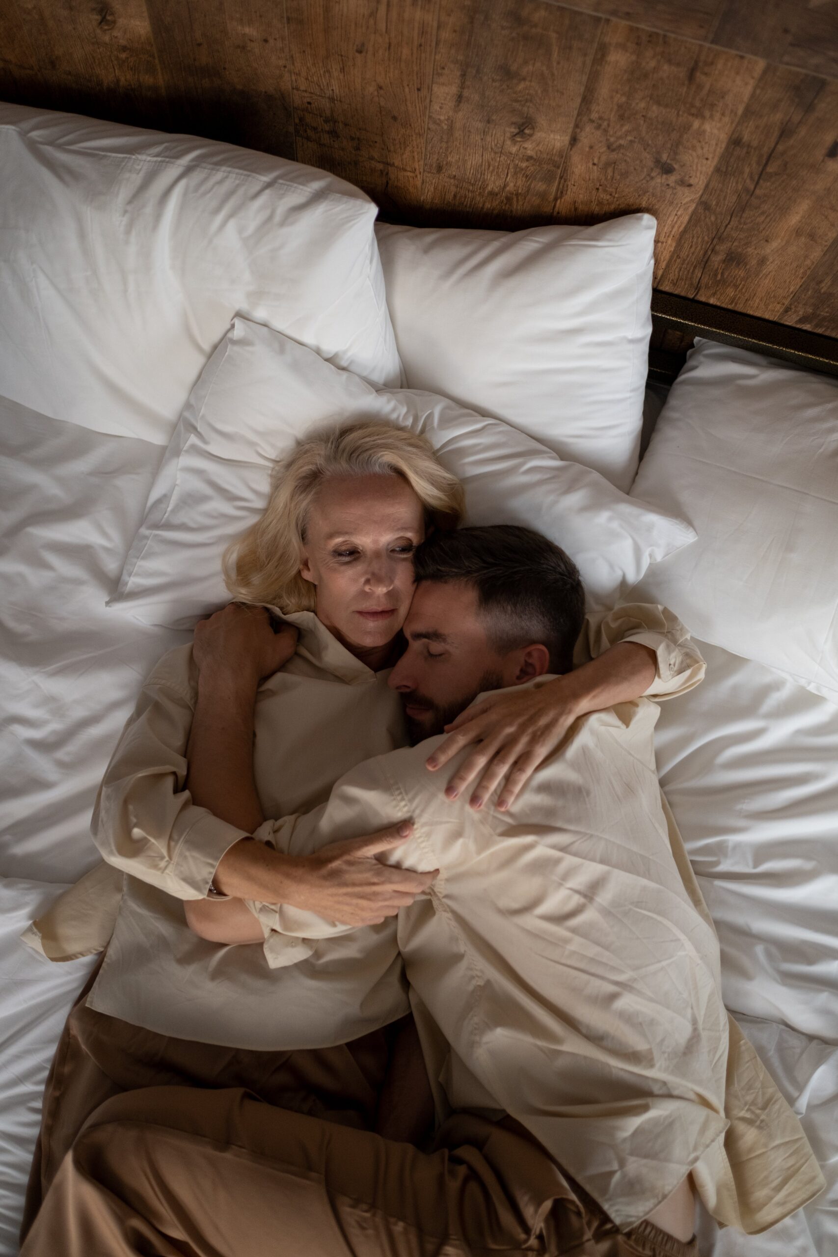 A photo of two people, a man and a woman, wearing beige clothes and cuddling in a white bed. Used as the featured image for GETSOME's post on how to unlearn and overcome feelings of sexual shame.